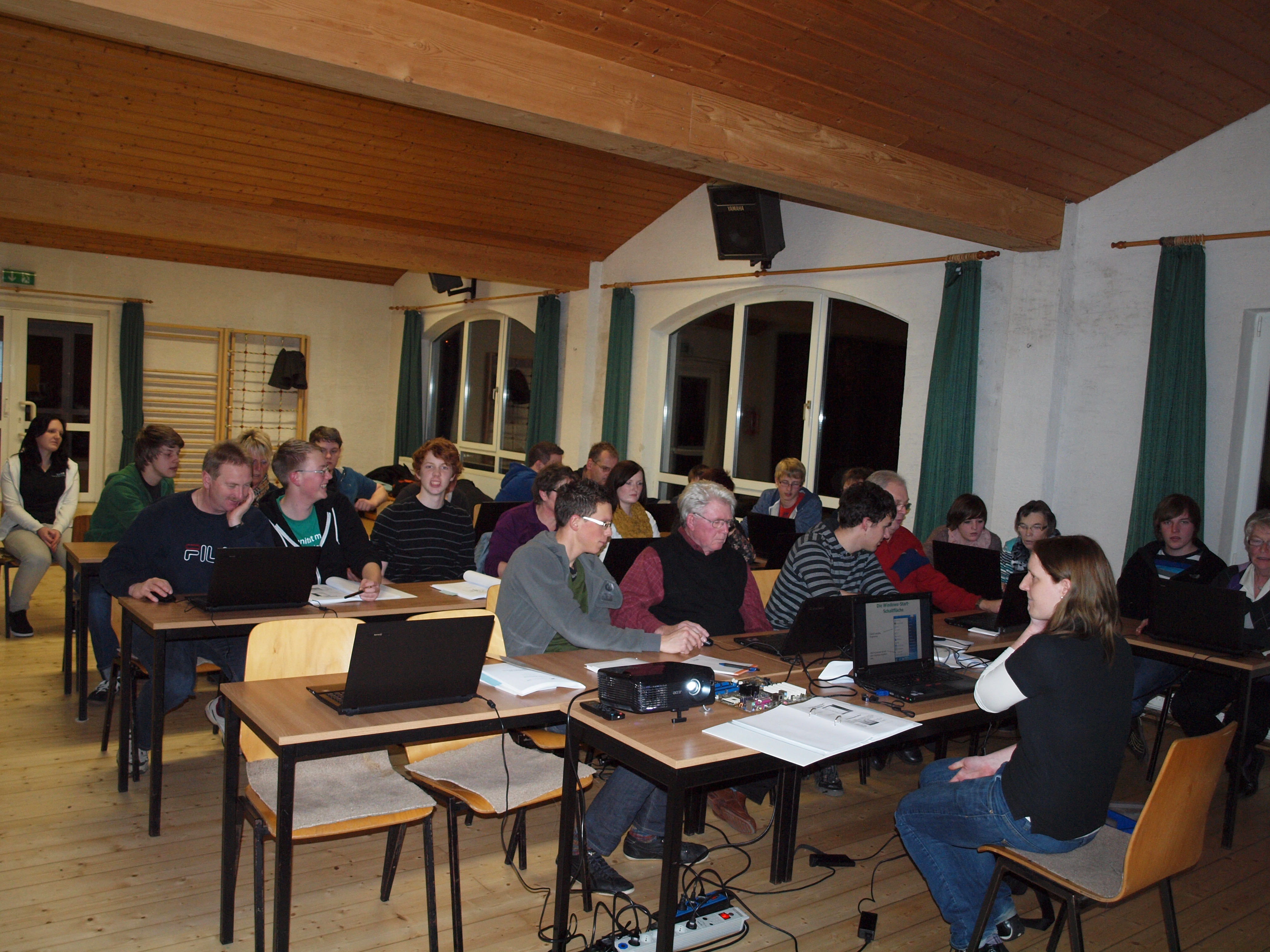 Junge und alte Menschen sitzen gemeinsam in einem Raum an Laptops