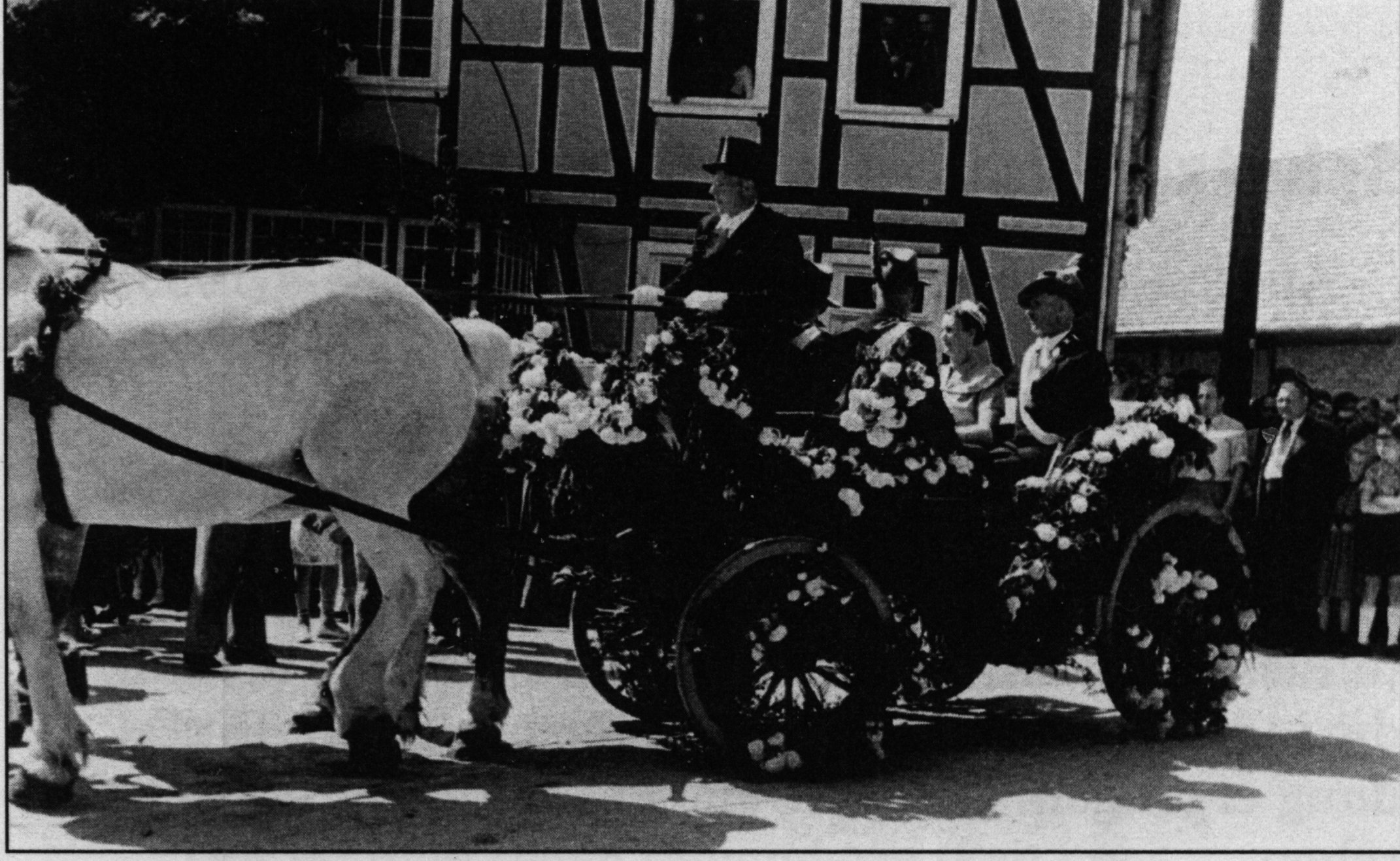 Eine festlich geschmückte Kutsche mit zwei Pferden. Darin sitzend das Schützenkönigspaar.