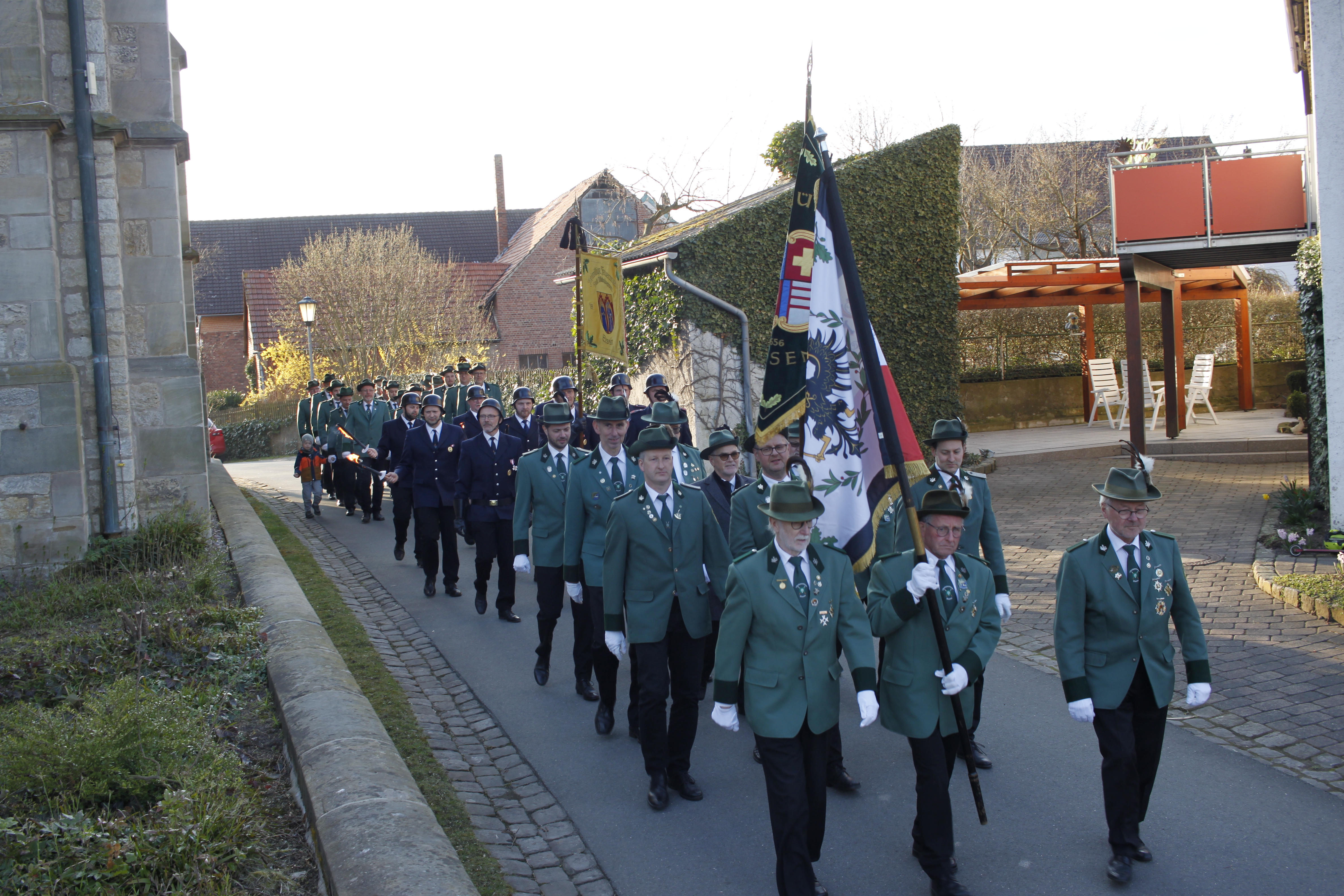 Schützen und Feuerwehrleute in Uniform und mit Fahnen marschieren über eine Straße