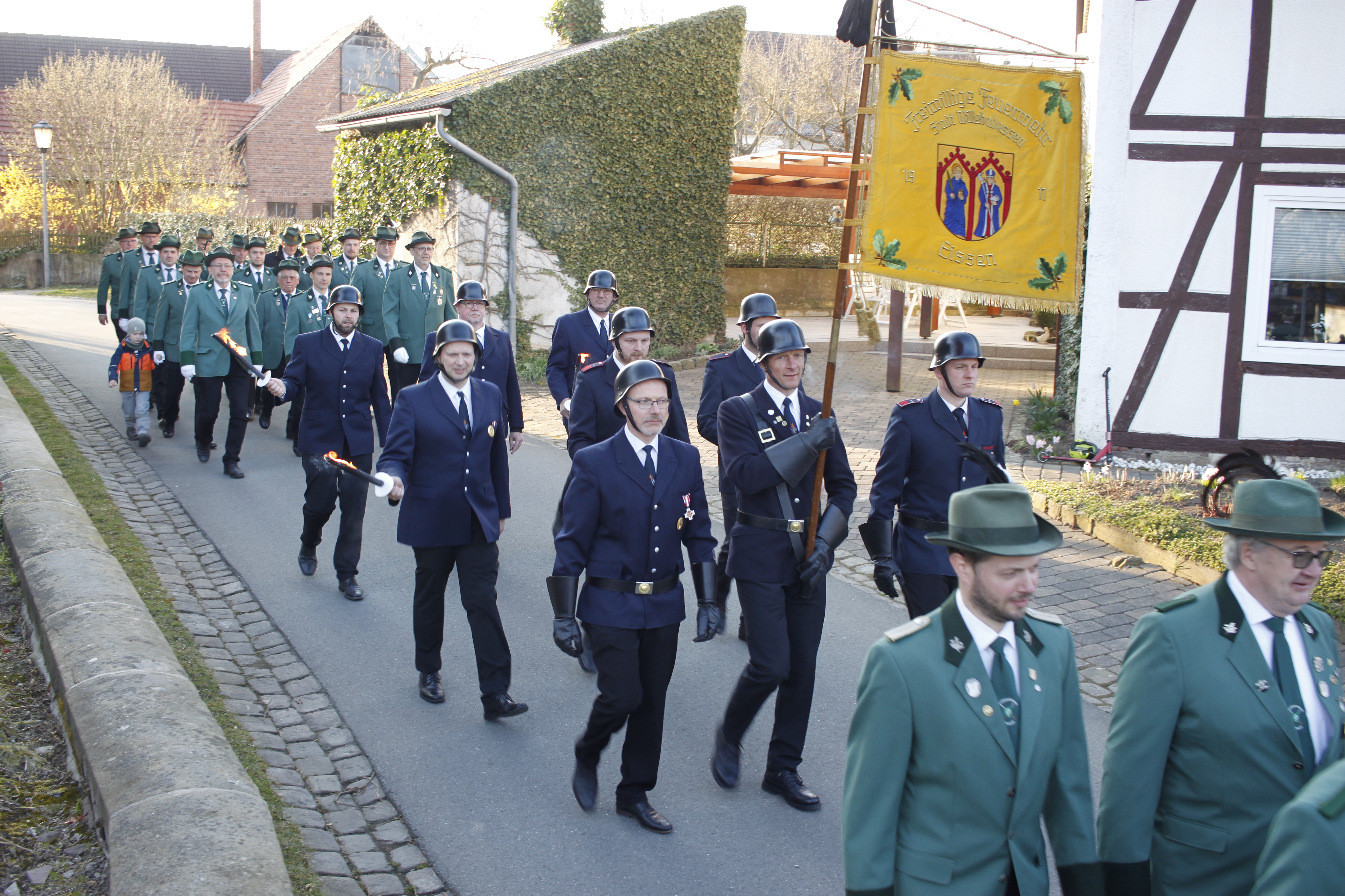 Schützen und Feuerwehrleute in Uniform und mit Fahnen marschieren über eine Straße